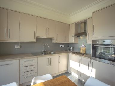 A kitchen with cabinets stove oven sink and dining table at Argoed in Abersoch