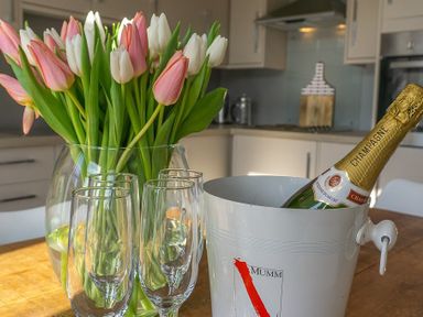 A kitchen table with a vase of pink and white tulips four champagne glasses and a champagne bottle in an ice bucket at Argoed in Abersoch