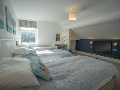 A bedroom with three beds a wall-mounted TV and a small desk with a stool at Argoed in Abersoch