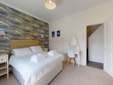 A bedroom with a bed towels bedside tables a dressing table and a chair at Argoed in Abersoch