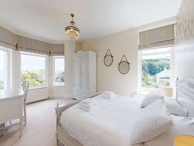 A bedroom with a white bed a wardrobe a desk with a chair and windows with striped blinds at Argoed in Abersoch