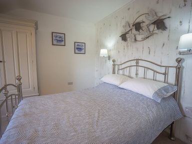 A bedroom with a metal bed frame pillows wall lamps and artwork at Argoed in Abersoch