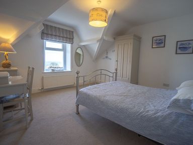 A bedroom with a metal bed frame a desk with a chair a wardrobe and a window with a striped blind at Argoed in Abersoch