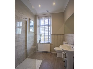 A bathroom with a walk-in shower a sink toilet a window with blinds and a plant on the sill at Argoed in Abersoch