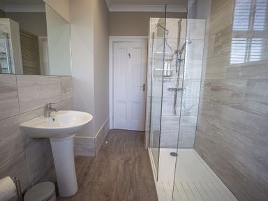 A bathroom with a pedestal sink a glass shower enclosure and a white door at Argoed in Abersoch