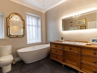A bathroom with a freestanding bathtub a toilet a wooden vanity with a sink and two mirrors at Argoed in Abersoch