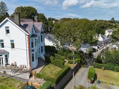 A white multi-story house with a garden and hedge near a street with trees and other buildings at Argoed in Abersoch