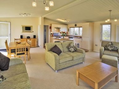 A living room and kitchen area with green sofas a wooden coffee table dining table and chairs at Arwelfa Lodge in Abersoch