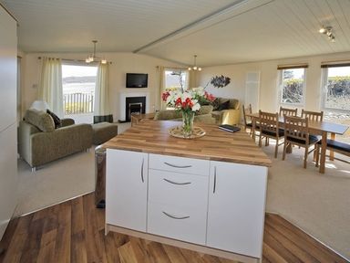 An open living and dining area with a kitchen island a sofa a dining table and windows at Arwelfa Lodge in Abersoch