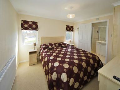 A bedroom with a double bed with polka dot bedding two windows bedside tables with lamps and an open door leading to a bathroom at Arwelfa Lodge in Abersoch