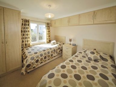 A bedroom with two single beds with polka dot bedding a window and wooden storage cabinets at Arwelfa Lodge in Abersoch