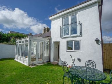 A white two-story house with a glass conservatory and a metal outdoor table and chairs on a lawn at Bryn Awel in Mynytho near Abersoch