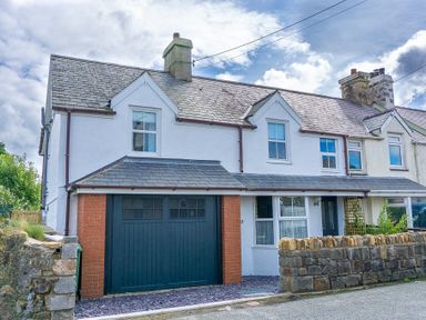A two-story white house with a slate roof garage with dark door and stone wall in front at Bryn Awel in Mynytho near Abersoch