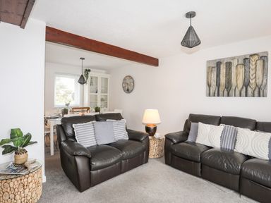 A living room with two brown leather sofas and cushions a lamp on a small table and a dining table visible in the background at Bywyd Da 232 Cae Du Abersoch