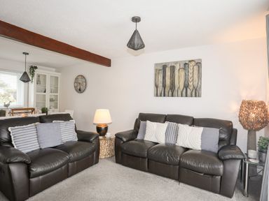 A living room with two black leather sofas and cushions at Bywyd Da 232 Cae Du in Abersoch
