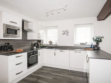A kitchen with white cabinets dark countertops and built in appliances at Bywyd Da 232 Cae Du in Abersoch