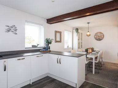 A kitchen with white cabinets and a dining area with a table set for six at Bywyd Da 232 Cae Du in Abersoch