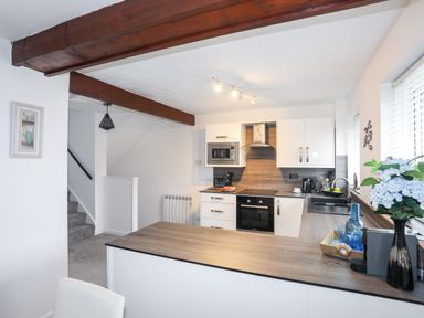 A kitchen with white cabinets wooden countertops a stove oven microwave and flowers on the counter at Bywyd Da 232 Cae Du in Abersoch