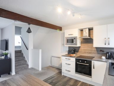 A kitchen area with white cabinets and appliances next to stairs at Bywyd Da 232 Cae Du in Abersoch