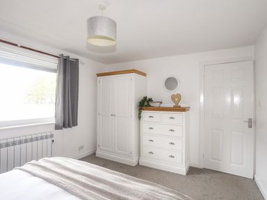 A bedroom with a white wardrobe and matching chest of drawers next to a closed door at Bywyd Da 232 Cae Du in Abersoch