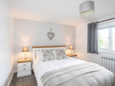 A bedroom with a double bed two bedside tables with lamps and a window with curtains at Bywyd Da (232 Cae Du) in Abersoch