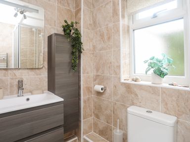 A bathroom with a sink and cabinet a toilet and window with a plant on the sill at Bywyd Da 232 Cae Du in Abersoch