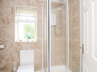 A bathroom with a toilet, a shower enclosure, a window with a plant, and tiled walls at Bywyd Da 232 Cae Du Abersoch