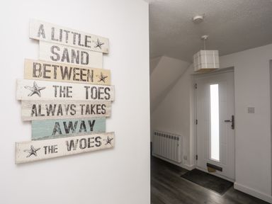 An entryway with a white door a wall-mounted radiator a ceiling light and a decorative wooden sign with text at Bywyd Da 232 Cae Du in Abersoch