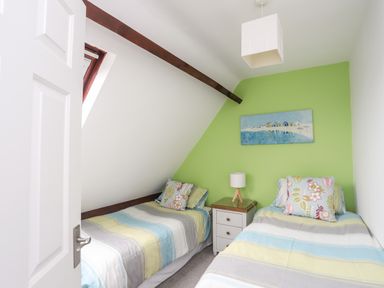 A bedroom with two single beds a bedside table and a lamp with striped bedding at Bywyd Da 232 Cae Du in Abersoch