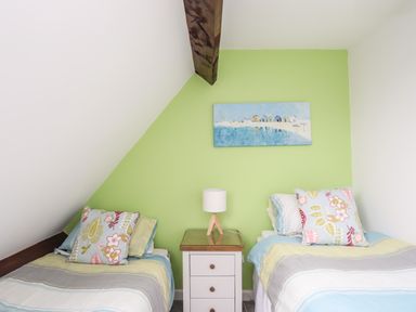 A bedroom with two single beds separated by a bedside table with a lamp and a painting on a green wall at Bywyd Da 232 Cae Du in Abersoch