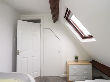 A bedroom with a chest of drawers a small plant a skylight window and two white doors at Bywyd Da (232 Cae Du) in Abersoch