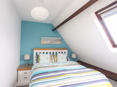 A bedroom with a double bed striped bedding bedside tables with lamps and a skylight window at Bywyd Da 232 Cae Du in Abersoch