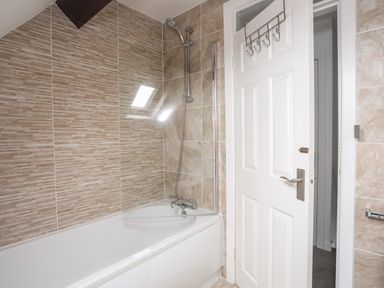 A bathroom with a bathtub shower combination a white door and beige tiled walls at Bywyd Da 232 Cae Du in Abersoch