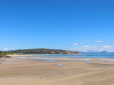 A sandy beach with some water pools and a headland with hills in the background at Bywyd Da 232 Cae Du in Abersoch