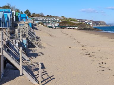A sandy beach with colorful beach huts on wooden stilts and stairs and buildings on a hill in the background at Bywyd Da 232 Cae Du in Abersoch