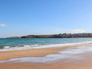 A sandy beach with waves and a view of hills and houses in the distance at Bywyd Da 232 Cae Du in Abersoch
