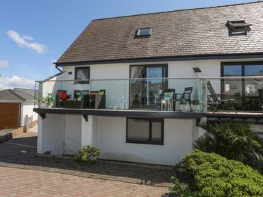 A house with a balcony with glass railing and outdoor furniture in front of a garage at Bywyd Da 232 Cae Du in Abersoch