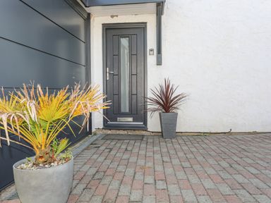 A front door with two potted plants on a brick driveway at Bywyd Da 232 Cae Du in Abersoch