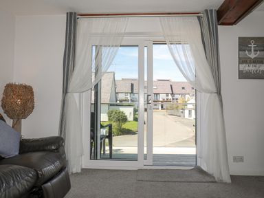 A sliding glass door with sheer curtains overlooking a street with houses at Bywyd Da (232 Cae Du) in Abersoch