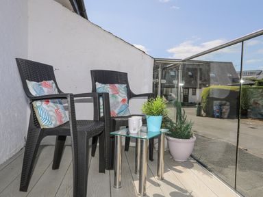 A balcony with two black chairs with cushions a small glass table with plants and mugs at Bywyd Da (232 Cae Du) in Abersoch