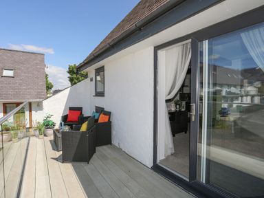 An outdoor balcony with black wicker chairs and colorful cushions with glass railing at Bywyd Da (232 Cae Du) in Abersoch