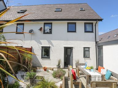 A backyard patio with wooden benches and a table set with fruit and drinks at Bywyd Da 232 Cae Du in Abersoch