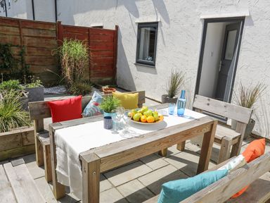 An outdoor patio with a wooden table and benches with colorful cushions at Bywyd Da 232 Cae Du in Abersoch