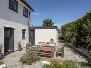 An outdoor patio with wooden seating and a table set with cushions and plants at Bywyd Da 232 Cae Du in Abersoch