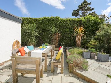 An outdoor patio with wooden benches and table with colorful cushions and plants in Abersoch