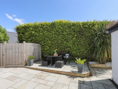An outdoor patio area with a table and chairs surrounded by plants and wooden fencing at Bywyd Da 232 Cae Du in Abersoch