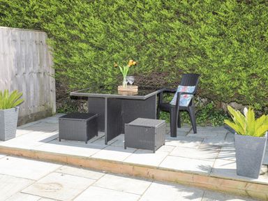 A patio area with a black wicker table and chairs with cushions and plants in pots at Bywyd Da 232 Cae Du Abersoch