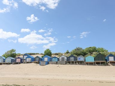 A row of wooden beach huts on sand dunes under a blue sky with clouds at Bywyd Da (232 Cae Du) in Abersoch