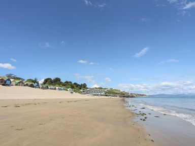 A sandy beach with colorful beach huts and calm sea water at Bywyd Da (232 Cae Du) in Abersoch