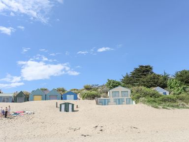 Beach huts on sand dunes with people on sandy beach and trees in the background at Bywyd Da (232 Cae Du) in Abersoch